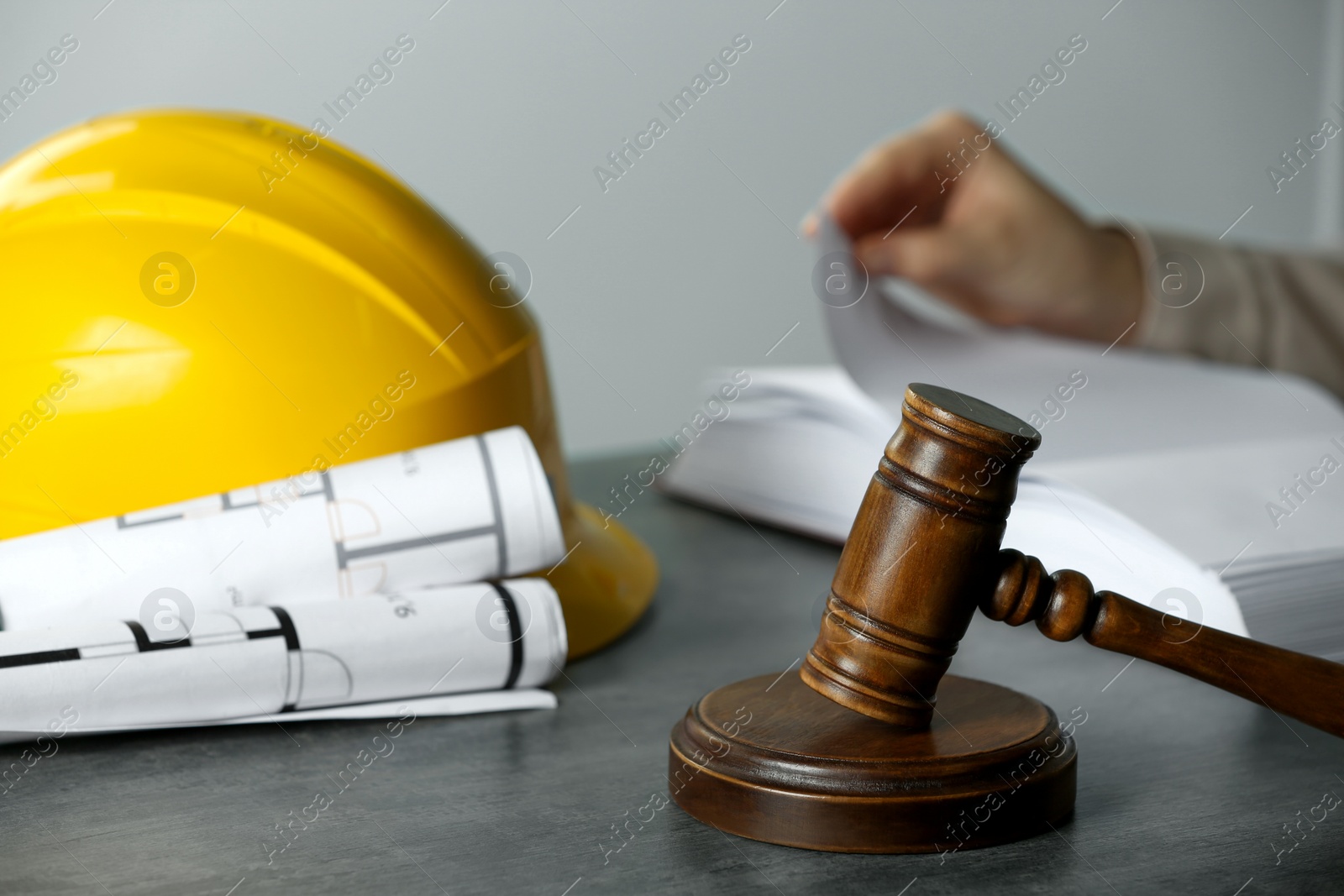 Photo of Construction and land law concepts. Woman reading book at grey table, focus on judge gavel