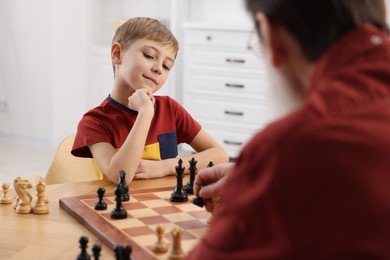 Photo of Little boy playing chess with his grandfather at table in room