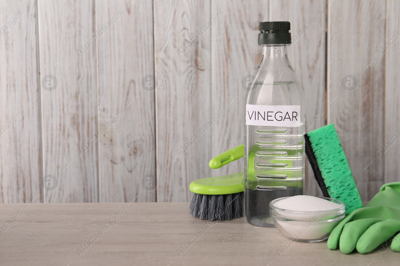 Photo of Natural cleaning products. Vinegar in bottle, baking soda, glove, sponge and brush on light wooden table. Space for text