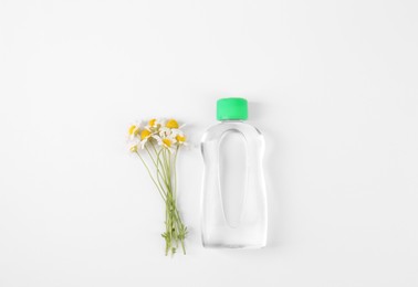 Transparent bottle with baby oil and daisies on white background, flat lay