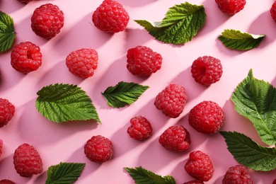 Photo of Tasty ripe raspberries and green leaves on pink background, flat lay