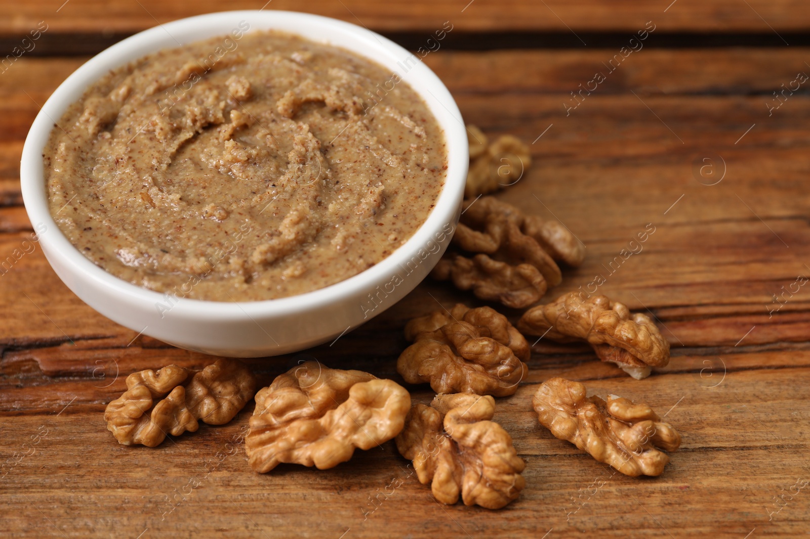 Photo of Delicious nut butter in bowl and walnuts on wooden table, closeup