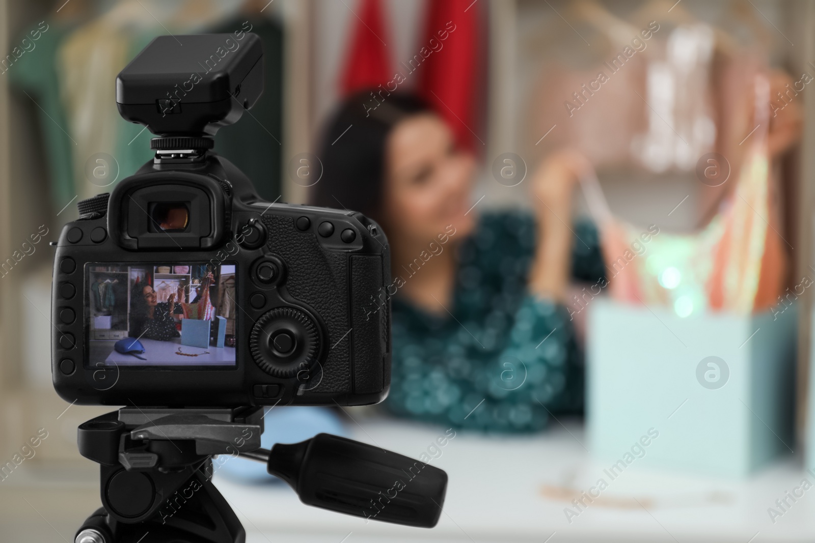 Photo of Fashion blogger recording new video at table indoors, focus on camera