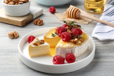 Photo of Brie cheese served with raspberries, walnuts and honey on white wooden table