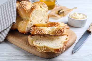 Photo of Cut freshly baked braided bread, knife and butter on white wooden table, closeup. Traditional Shabbat challah