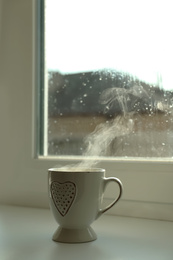 Cup of hot drink near window on rainy day. Space for text