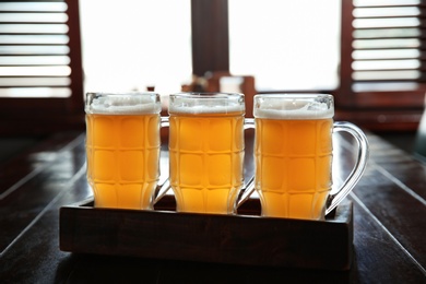 Glasses of tasty beer on wooden table in bar
