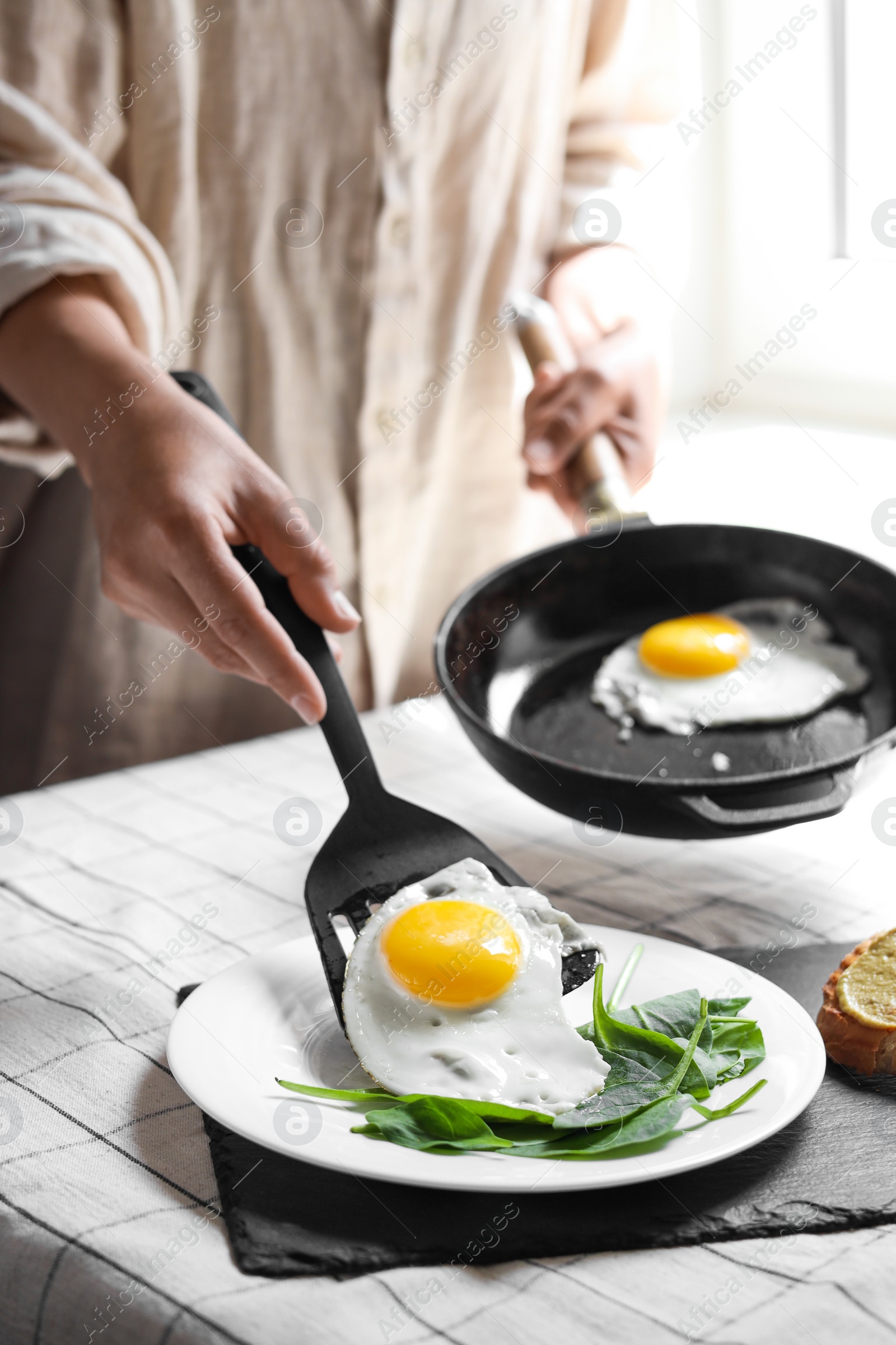 Photo of Woman putting tasty fried eggs onto plate at table indoors, closeup