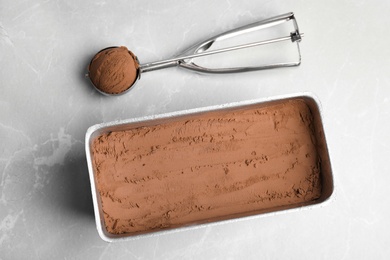 Photo of Container and scoop with chocolate ice cream on grey table, flat lay