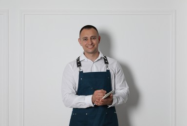 Portrait of happy young waiter with notebook near white wall
