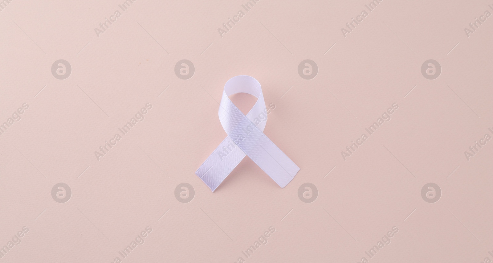 Photo of White awareness ribbon on beige background, top view