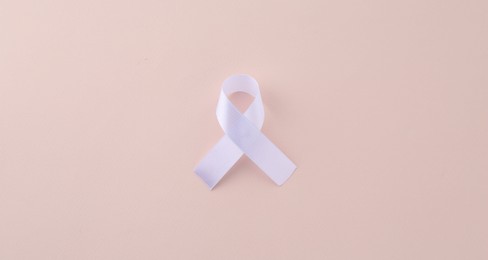 White awareness ribbon on beige background, top view