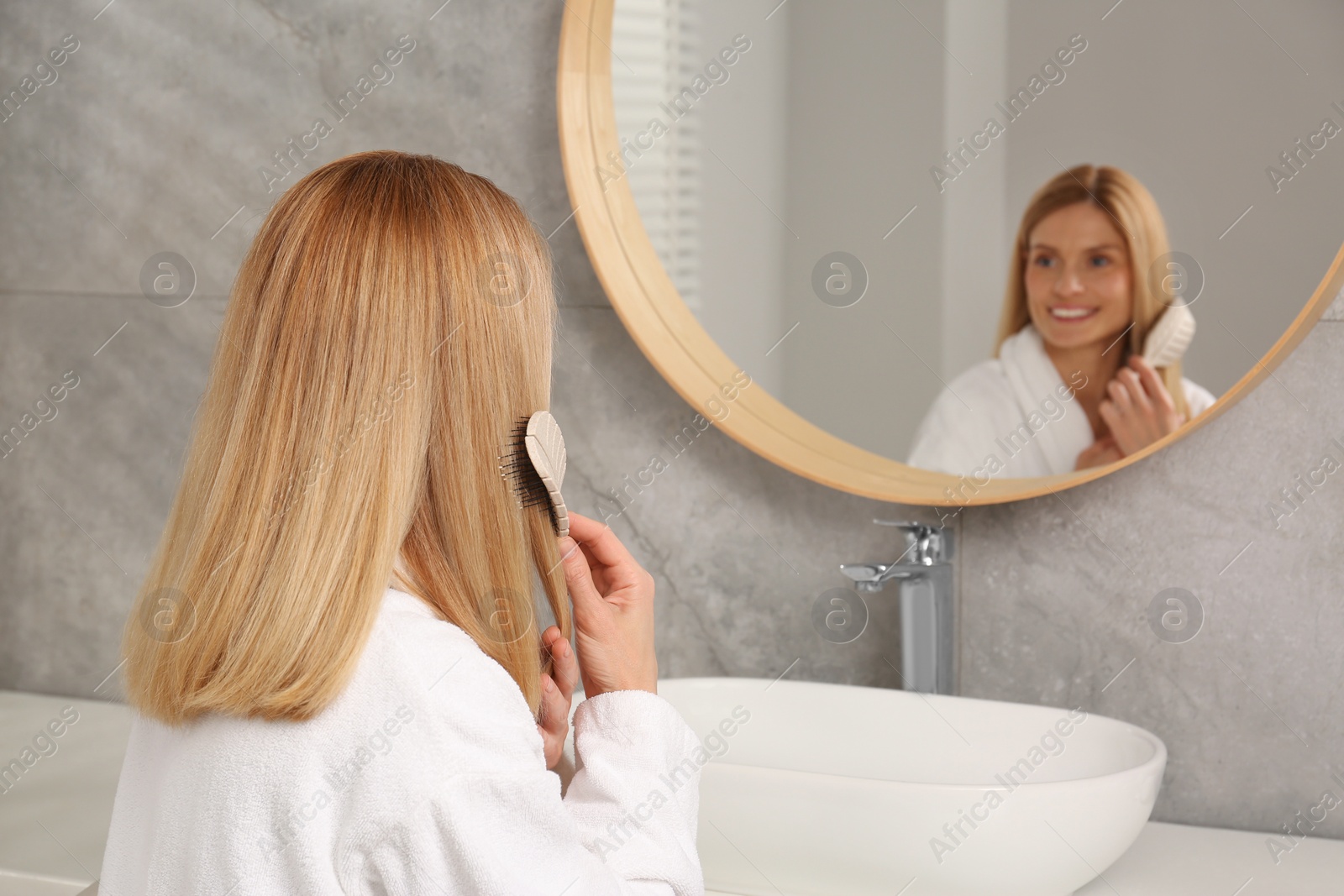 Photo of Beautiful woman brushing her hair near mirror in bathroom