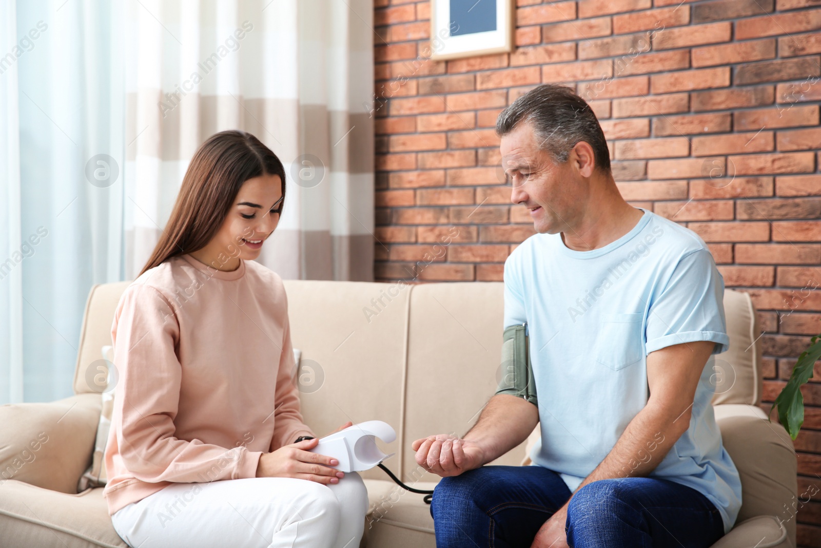 Photo of Young woman checking mature man's pulse with medical device at home