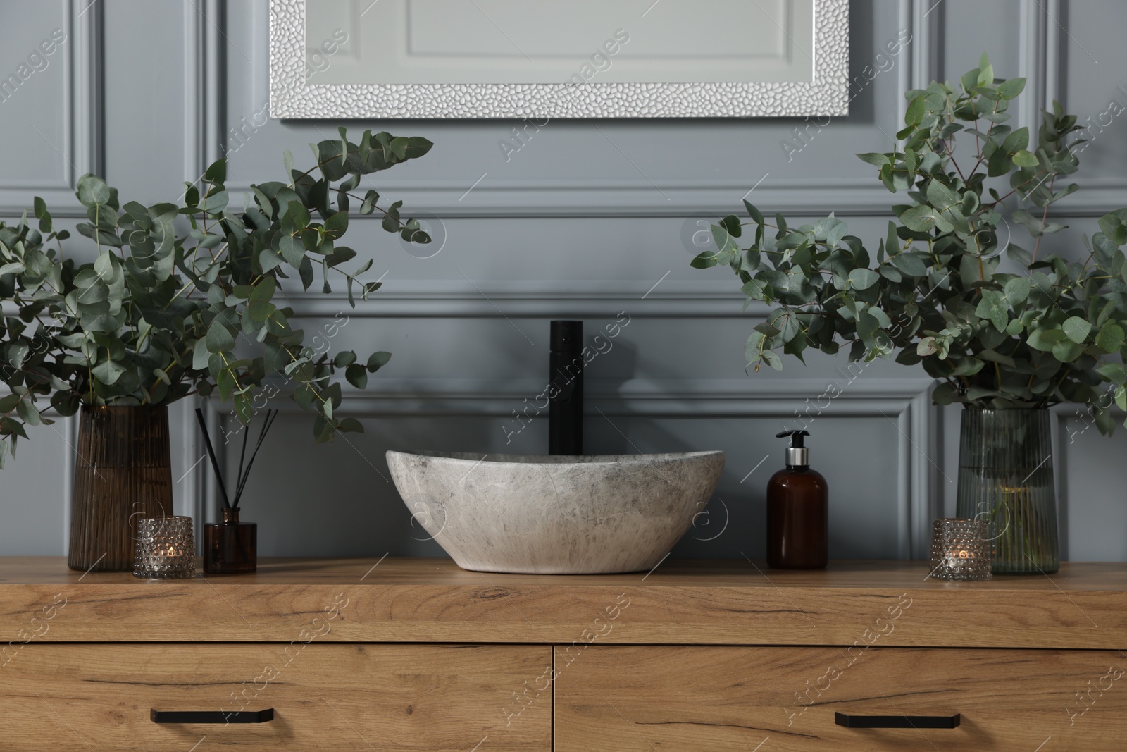 Photo of Eucalyptus branches, aroma sticks and candles near vessel sink on bathroom vanity. Interior design