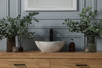 Photo of Eucalyptus branches, aroma sticks and candles near vessel sink on bathroom vanity. Interior design