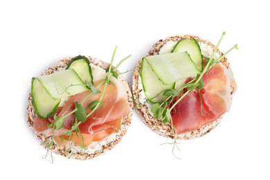 Photo of Crunchy buckwheat cakes with cream cheese, prosciutto and cucumber slices on white background, top view