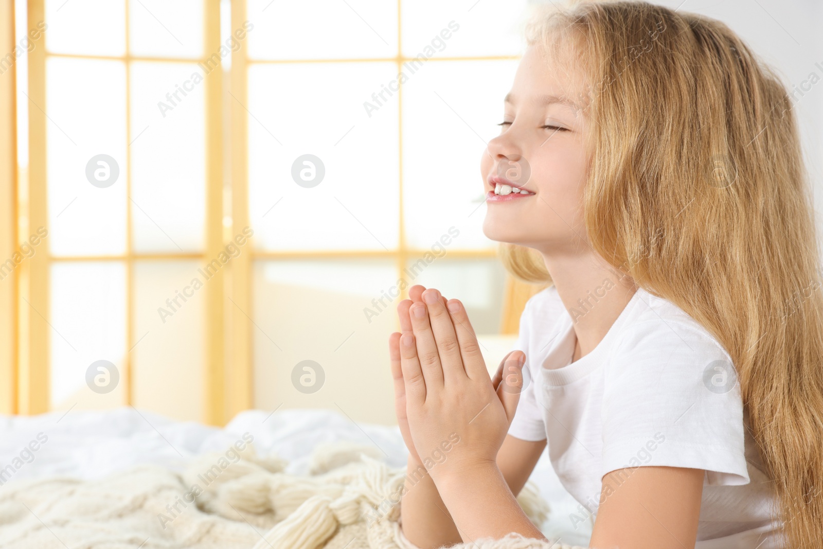 Photo of Girl with clasped hands praying on bed at home, space for text