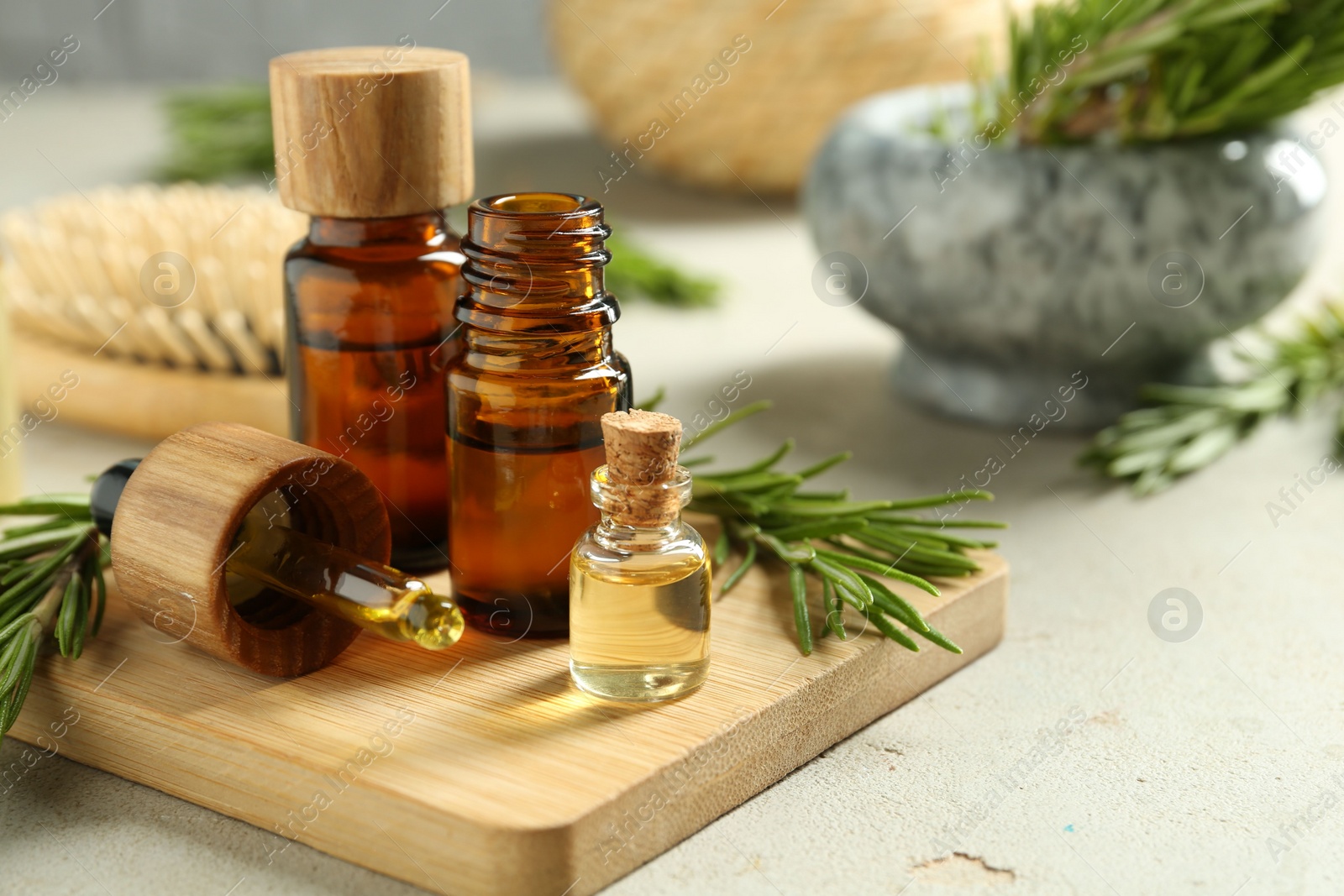 Photo of Essential oils in bottles and rosemary on light gray table, closeup