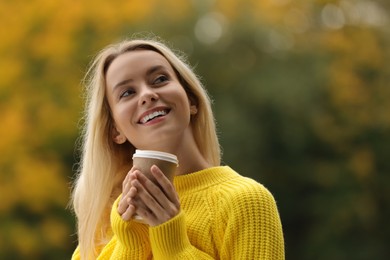 Autumn vibes. Portrait of happy woman with paper cup outdoors. Space for text