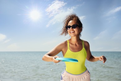 Photo of Happy African American woman throwing flying disk at beach on sunny day