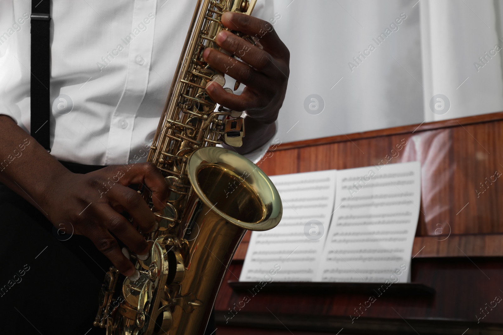 Photo of African-American man playing saxophone indoors, closeup with space for text. Talented musician