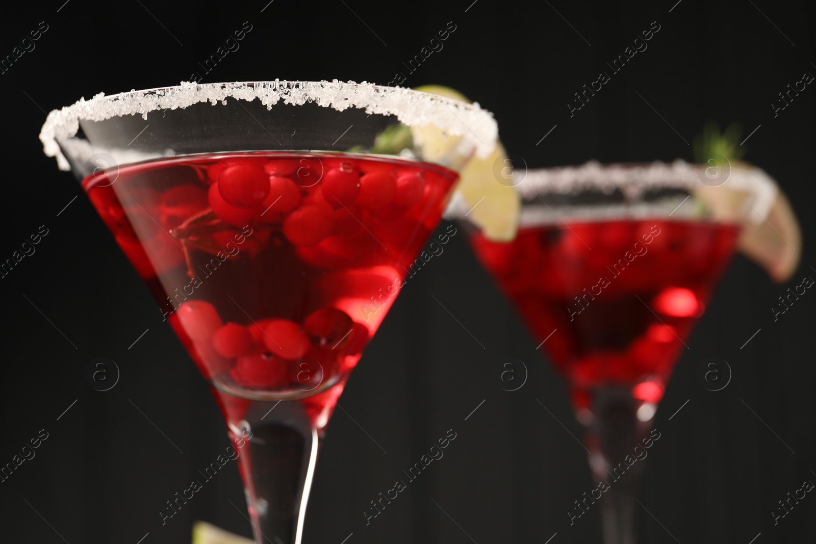 Photo of Tasty cranberry cocktail in glasses against black background, closeup