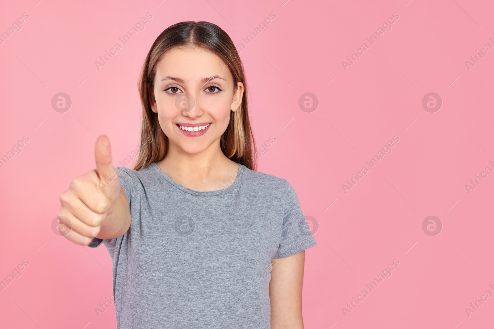 Photo of Teenage girl showing thumb up on pink background. Space for text