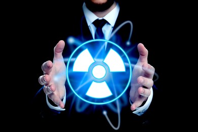 Man holding glowing atom symbol with radiation warning sign on black background, closeup