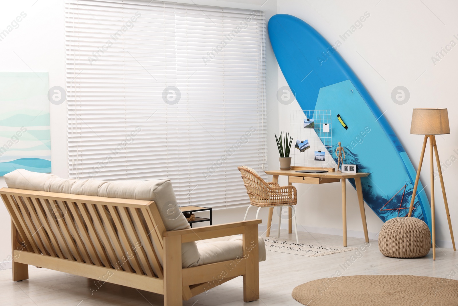 Photo of SUP board, workplace and sofa in room. Interior design