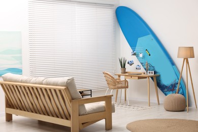 Photo of SUP board, workplace and sofa in room. Interior design