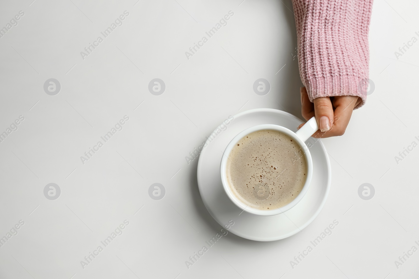 Photo of Woman holding cup of coffee at white table, top view. Space for text