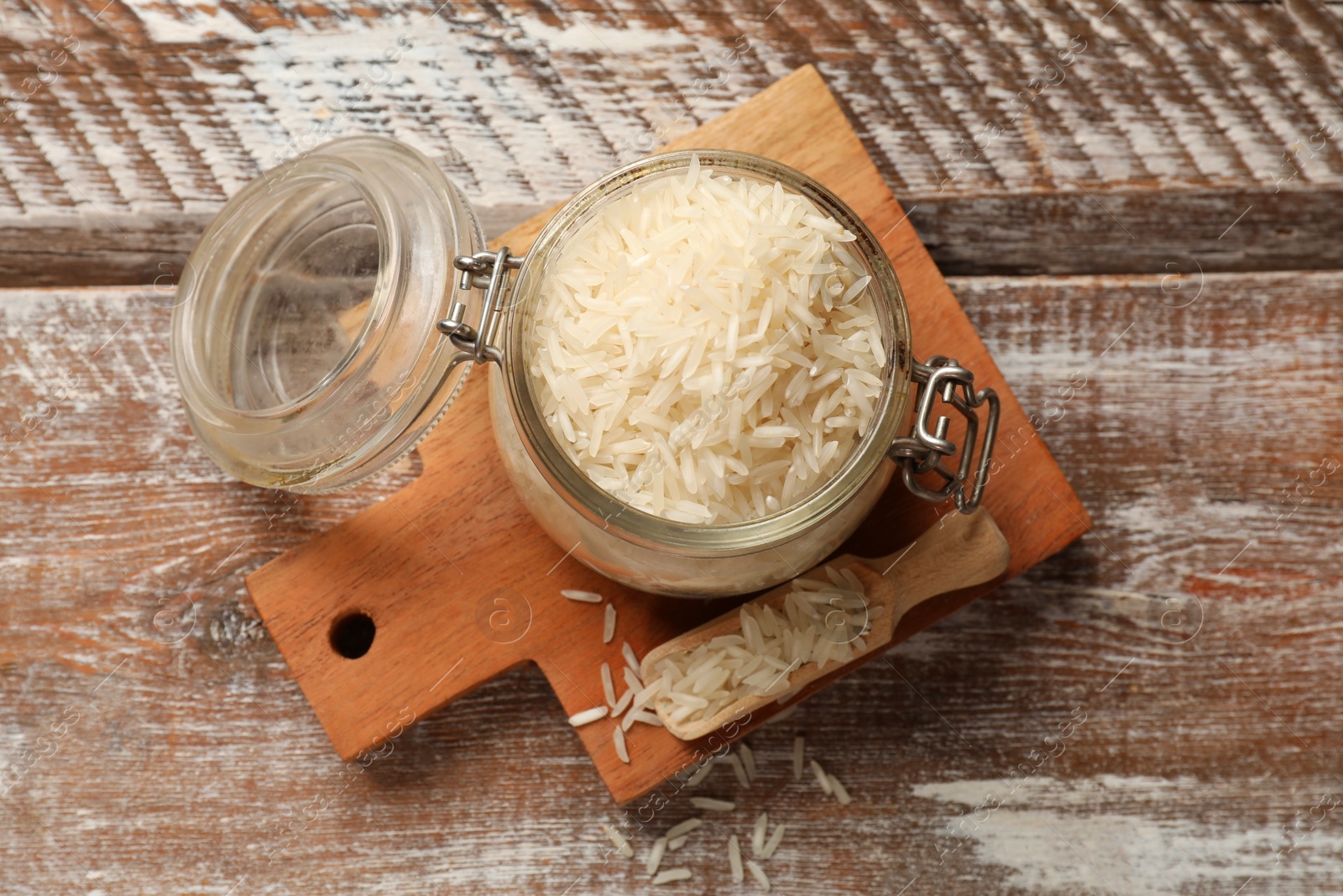 Photo of Raw basmati rice in glass jar and scoop on wooden table, top view