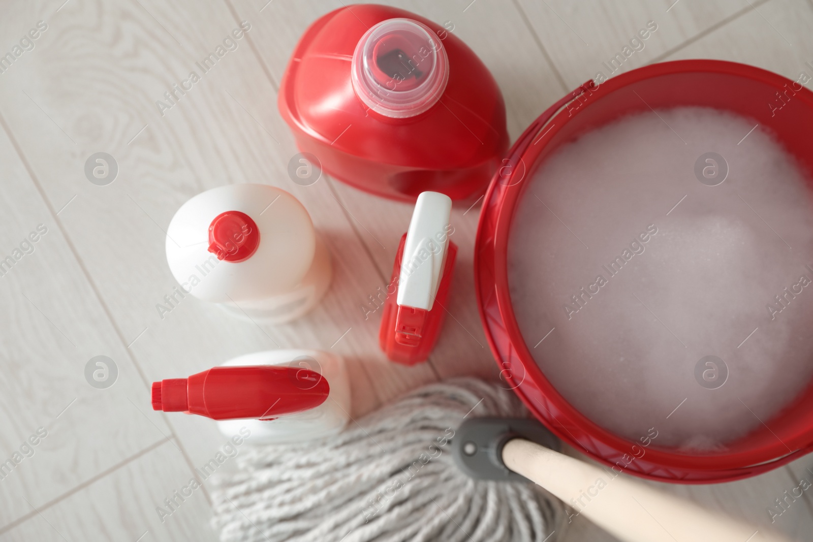 Photo of Bucket, mop and different cleaning products on floor indoors, flat lay