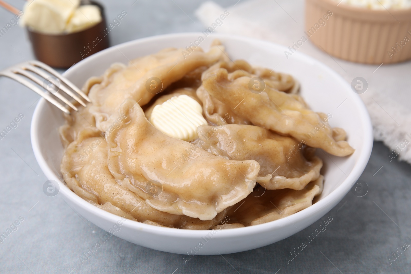 Photo of Delicious dumplings (varenyky) with cottage cheese and butter served on light grey table, closeup