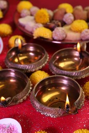 Photo of Diwali celebration. Diya lamps on shiny red table, closeup