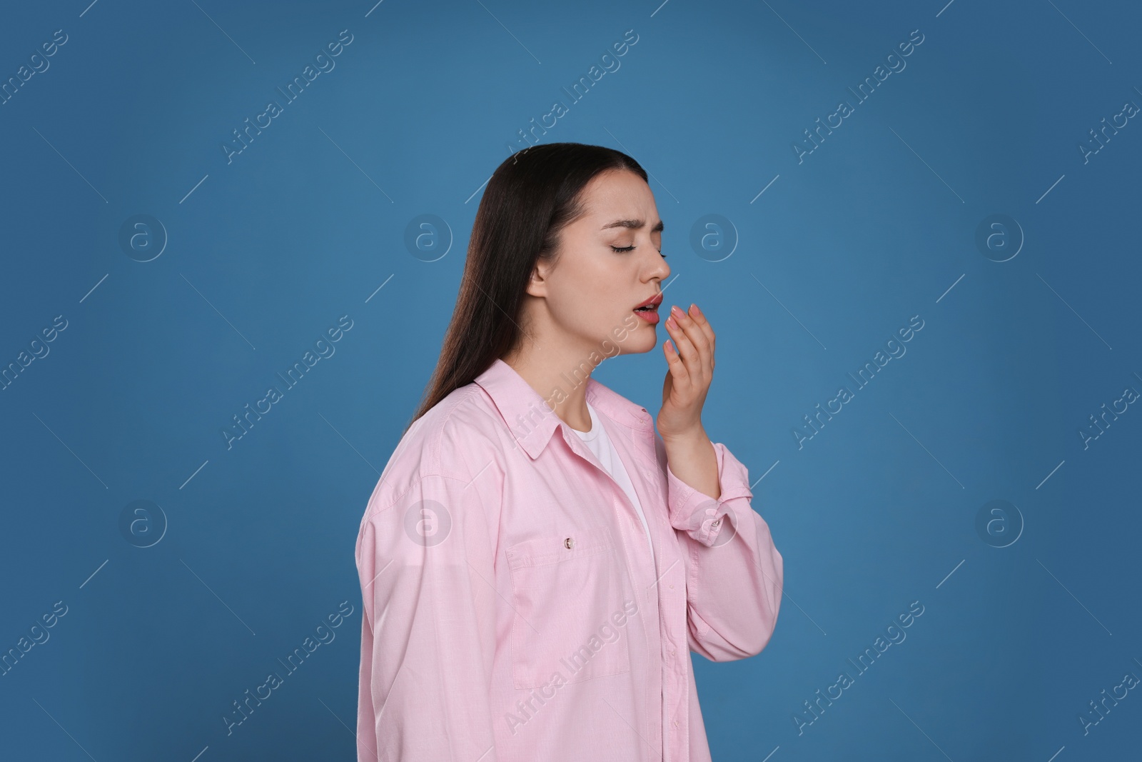 Photo of Young woman sneezing on blue background. Cold symptoms