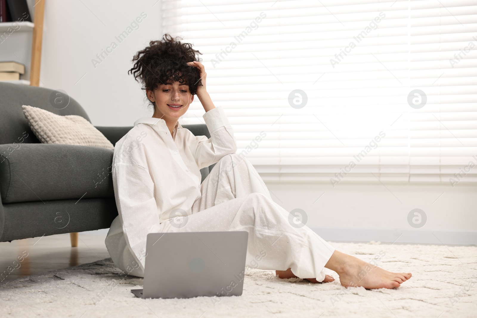 Photo of Beautiful young woman in stylish pyjama using laptop on floor at home