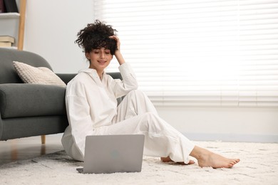 Photo of Beautiful young woman in stylish pyjama using laptop on floor at home