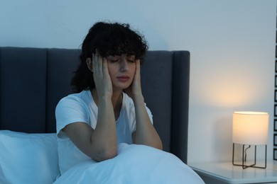 Photo of Young woman suffering from headache in bed at night