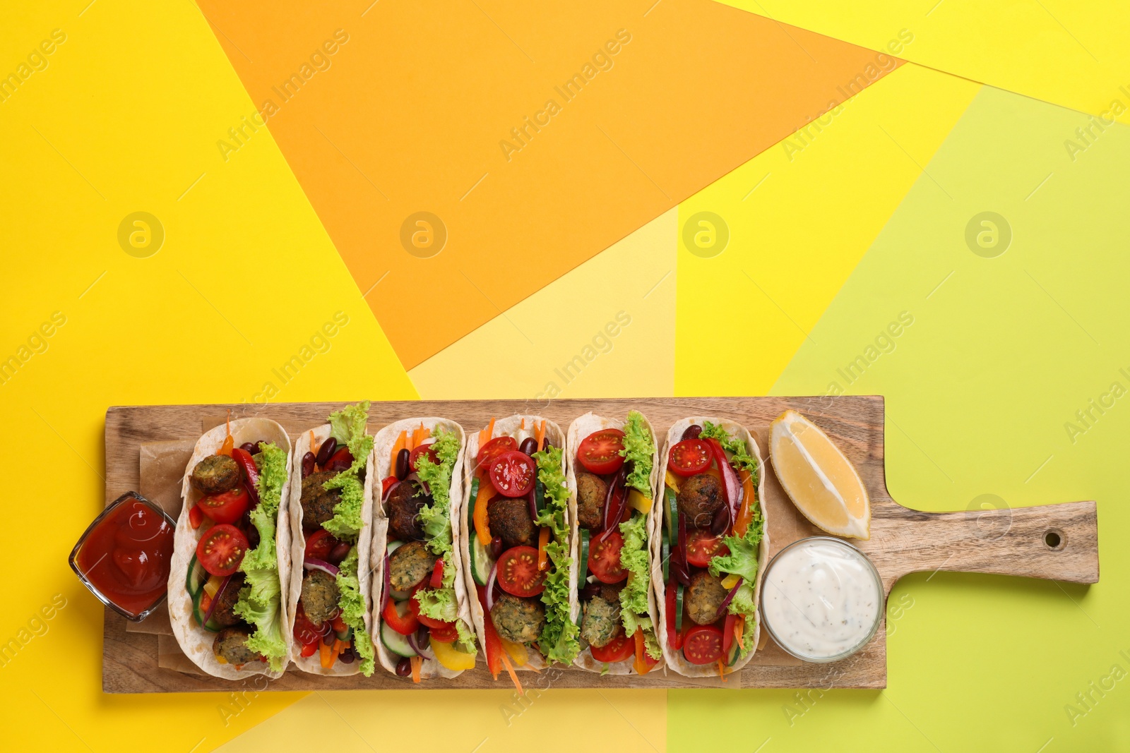 Photo of Many delicious vegetarian tacos served on yellow table, top view. Space for text