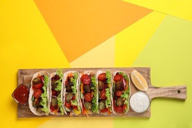 Many delicious vegetarian tacos served on yellow table, top view. Space for text
