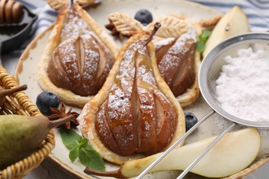 Photo of Delicious pears baked in puff pastry with powdered sugar served on table, closeup