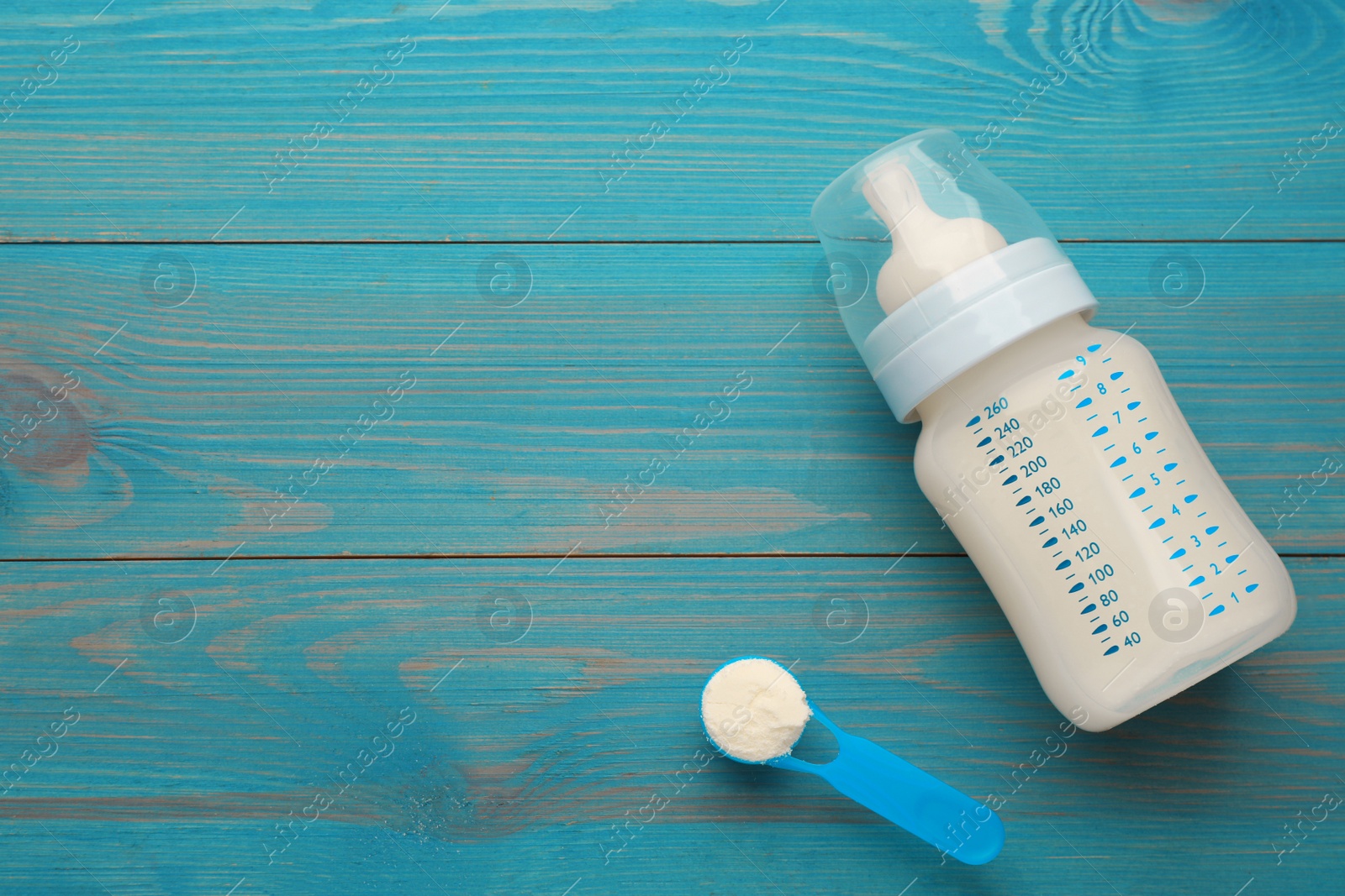 Photo of Feeding bottle with infant formula and powder on light blue wooden table, flat lay. Space for text