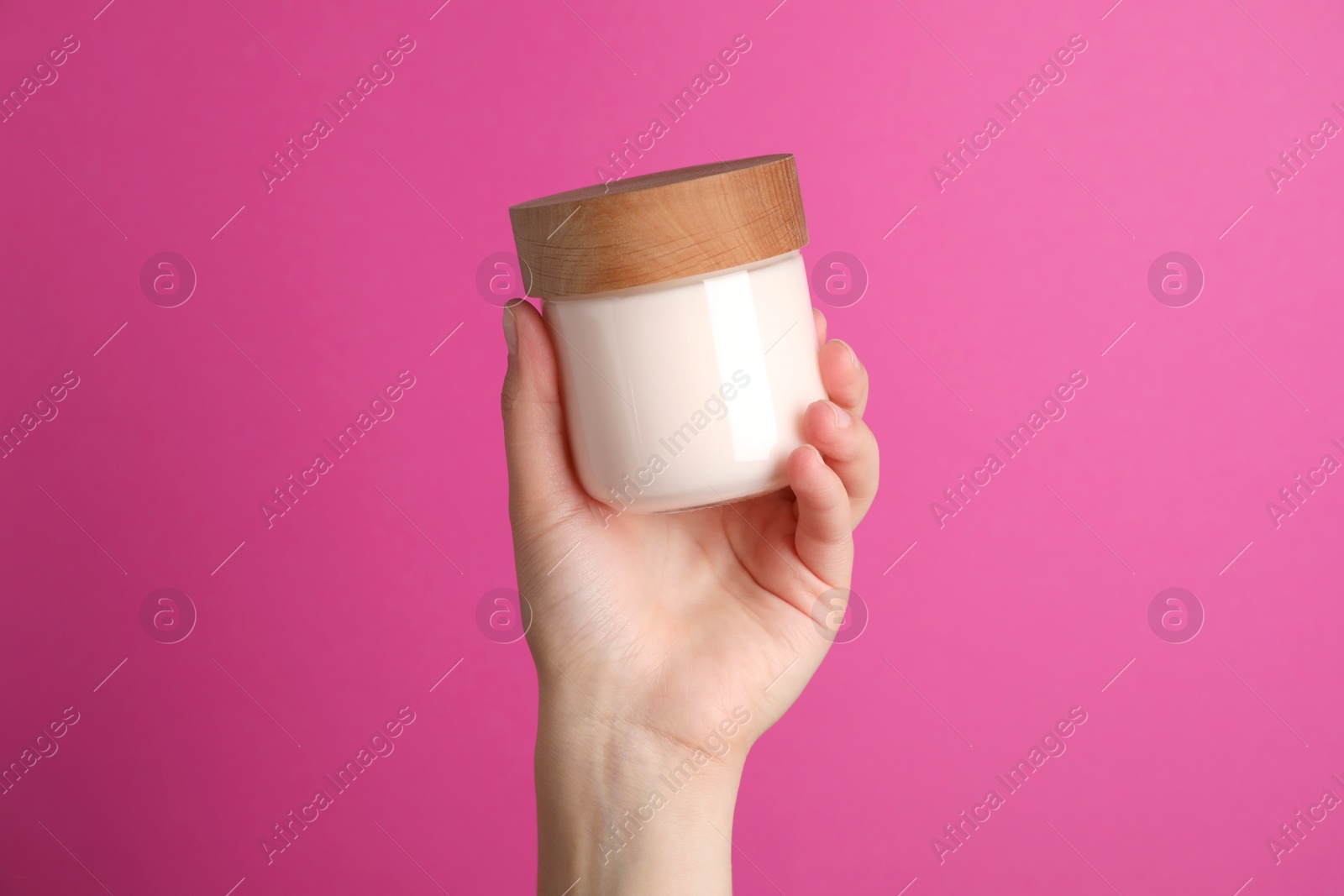 Photo of Woman holding jar of face cream on pink background, closeup