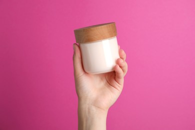 Woman holding jar of face cream on pink background, closeup