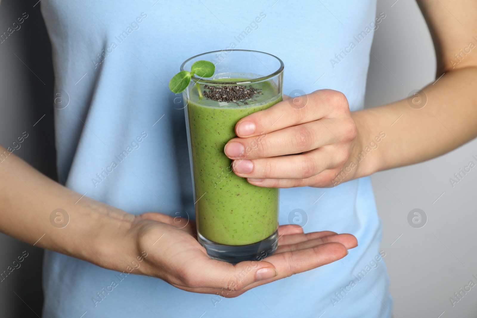 Photo of Woman holding glass of fresh green smoothie with chia seeds on grey background, closeup