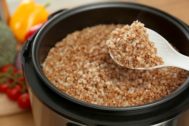Photo of Spoon with delicious buckwheat over multi cooker in kitchen, closeup