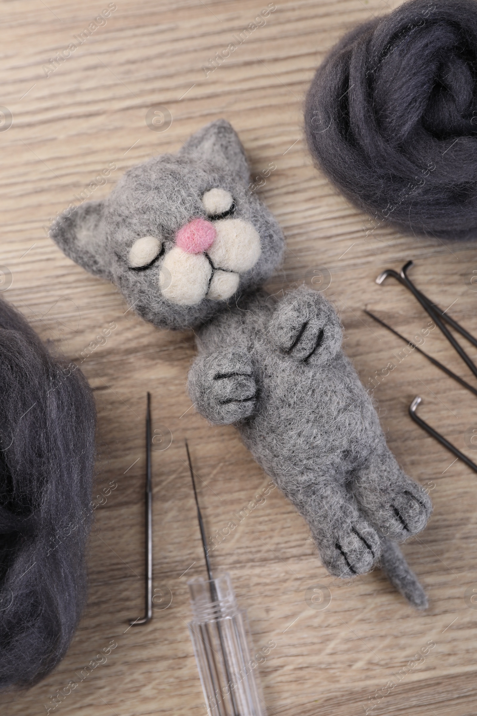 Photo of Felted cat, wool and tools on wooden table, flat lay