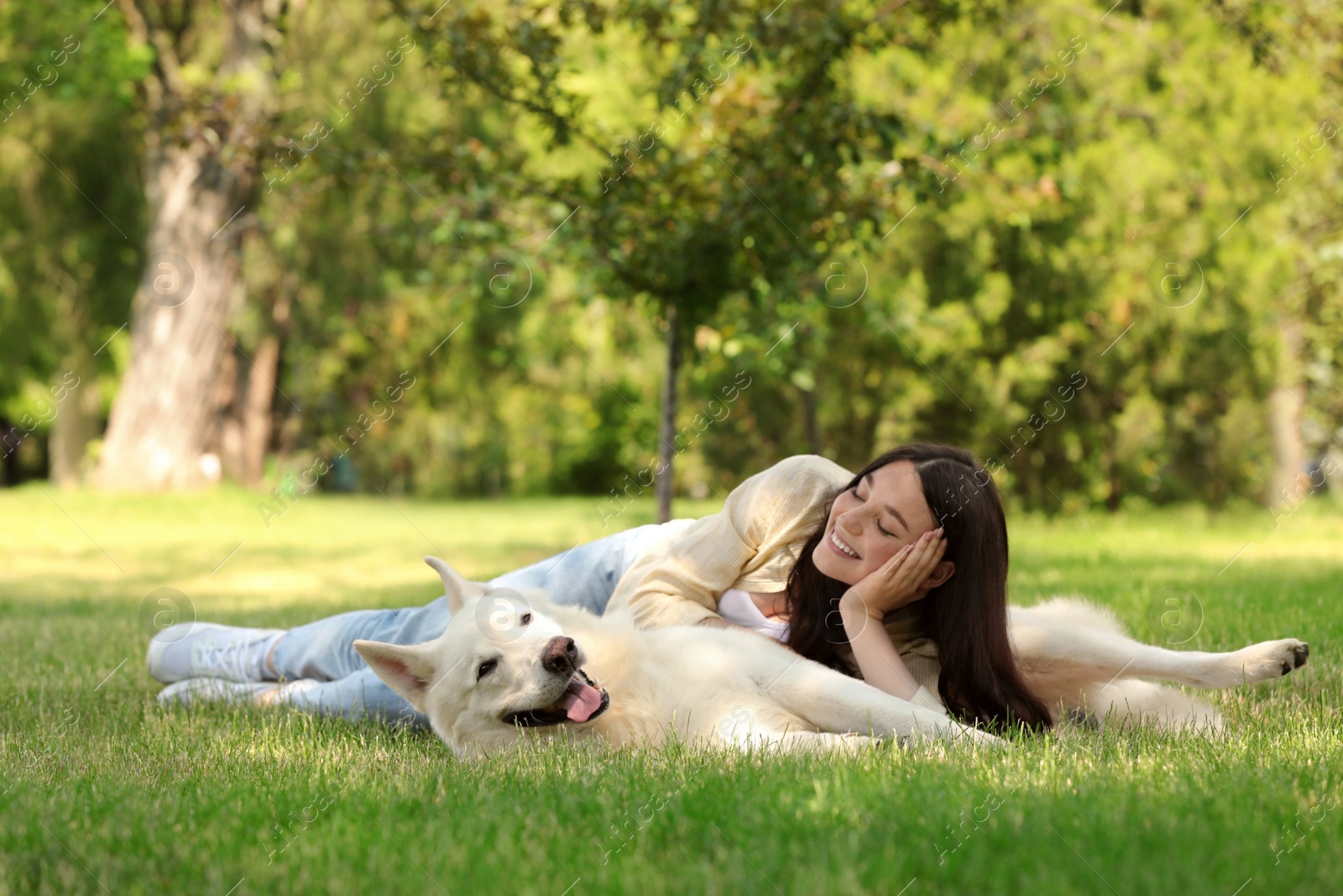 Photo of Teenage girl lying with her white Swiss Shepherd dog on green grass in park